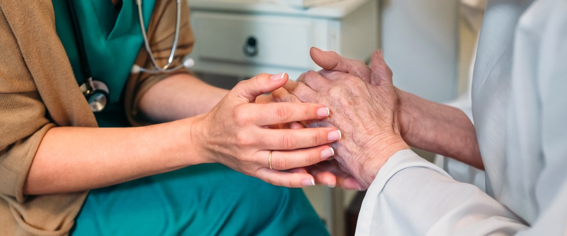 Female doctor giving encouragement to elderly patient by holding her hands